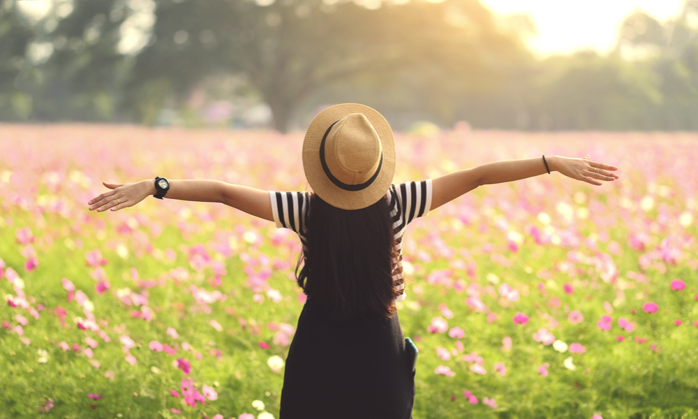 A woman standing in a meadow with her arms spread out.